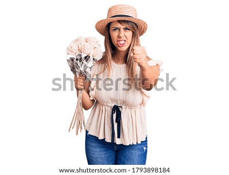 Young beautiful woman wearing hat holding bouquet of flowers annoyed and frustrated shouting with anger, yelling crazy with anger and hand raised 
