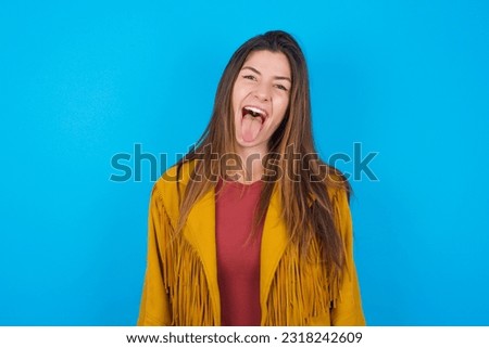 young beautiful woman wearing jacket over blue studio background with happy and funny face smiling and showing tongue.