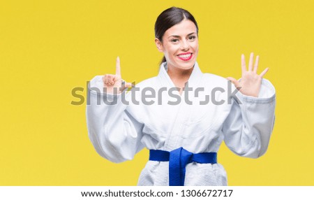 Young beautiful woman wearing karate kimono uniform over isolated background showing and pointing up with fingers number seven while smiling confident and happy.