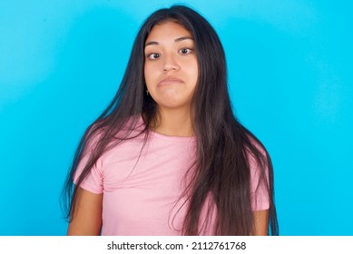 Young beautiful woman wearing pink T-shirt against blue background making grimace and crazy face, screaming out of control, funny lunatic expressing freedom and wild.