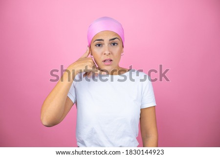Young beautiful woman wearing pink headscarf over isolated pink background confused doing phone gesture with hand and fingers like talking on the telephone