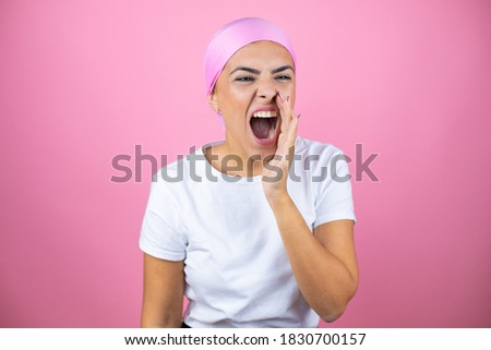 Young beautiful woman wearing pink headscarf over isolated pink background shouting and screaming loud to side with hand on mouth