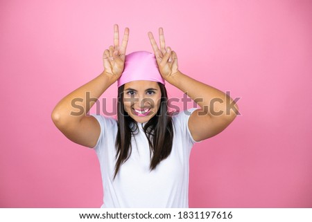 Young beautiful woman wearing pink headscarf over isolated pink background Posing funny and crazy with fingers on head as bunny ears, smiling cheerful