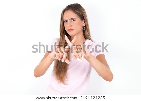 young beautiful woman wearing pink T-shirt over white background  has rejection angry expression crossing fingers doing negative sign.