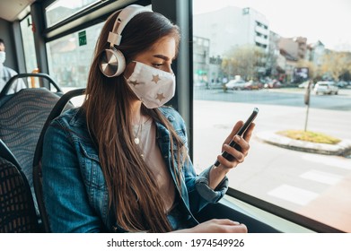 Young beautiful woman wearing protective mask and using a smartphone while riding a bus with a headphones on her head