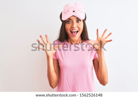 Young beautiful woman wearing sleep mask standing over isolated white background celebrating crazy and amazed for success with arms raised and open eyes screaming excited. Winner concept
