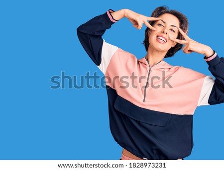 Young beautiful woman wearing sportswear doing peace symbol with fingers over face, smiling cheerful showing victory 