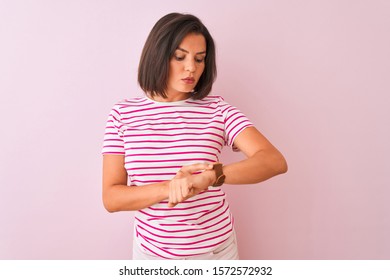 Young beautiful woman wearing striped t-shirt standing over isolated pink background Checking the time on wrist watch, relaxed and confident