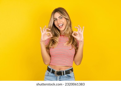 Young beautiful woman wearing striped t-shirt over yellow background  showing both hands with fingers in OK sign. Approval or recommending concept - Powered by Shutterstock