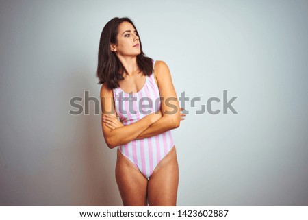 Young beautiful woman wearing striped pink swimsuit swimwear over isolated background looking to the side with arms crossed convinced and confident