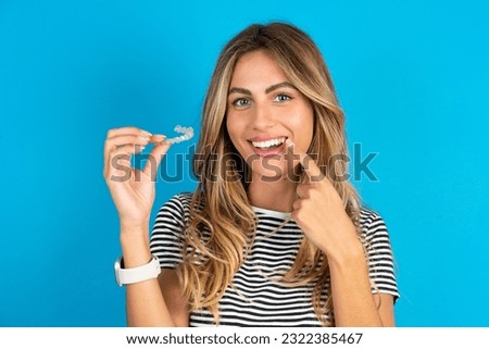 Young beautiful woman wearing striped t-shirt  holding an invisible aligner and pointing to her perfect straight teeth. Dental healthcare and confidence concept.