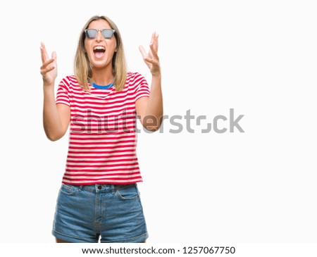 Young beautiful woman wearing sunglasses over isolated background crazy and mad shouting and yelling with aggressive expression and arms raised. Frustration concept.