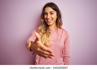 Young beautiful woman wearing a sweater over pink isolated background smiling friendly offering handshake as greeting and welcoming. Successful business. - Shutterstock ID 1452693047
