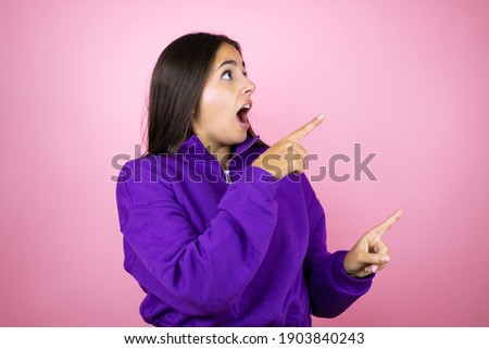 Young beautiful woman wearing sweatshirt over isolated pink background surprised and pointing her fingers side