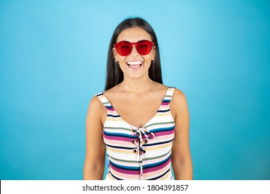 Young beautiful woman wearing swimsuit and sunglasses over isolated blue background smiling