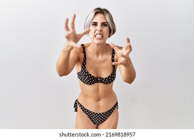 Young beautiful woman wearing swimsuit over isolated background shouting frustrated with rage, hands trying to strangle, yelling mad 