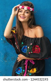 Young beautiful woman wearing traditional mexican dress is posing beside blue concrete wall
