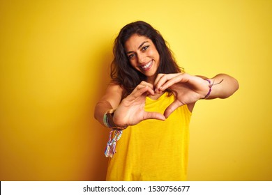 Young beautiful woman wearing t-shirt standing over isolated yellow background smiling in love showing heart symbol and shape with hands. Romantic concept.