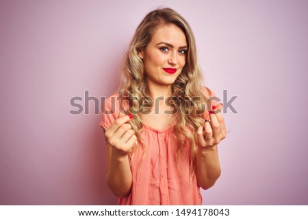 Young beautiful woman wearing t-shirt standing over pink isolated background doing money gesture with hands, asking for salary payment, millionaire business
