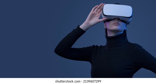 Young beautiful woman wearing a VR headset and experiencing virtual reality, futuristic technology concept - Shutterstock ID 2139607299