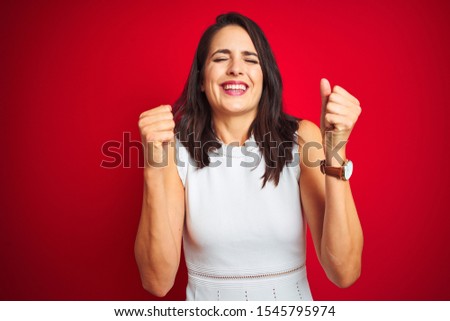 Young beautiful woman wearing white dress standing over red isolated background excited for success with arms raised and eyes closed celebrating victory smiling. Winner concept.