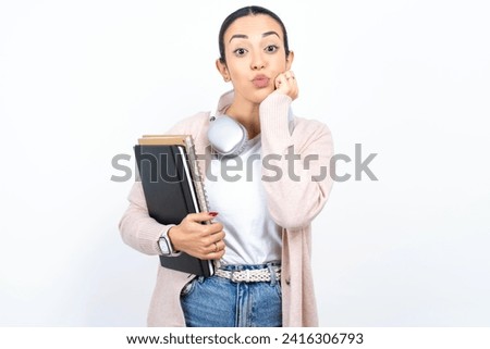 Young beautiful woman wearing white sweater with surprised expression keeps hands under chin keeps lips folded makes funny grimace