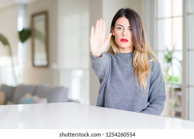 Young beautiful woman wearing winter sweater at home doing stop sing with palm of the hand. Warning expression with negative and serious gesture on the face.