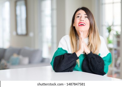 Young beautiful woman wearing winter sweater at home begging and praying with hands together with hope expression on face very emotional and worried. Asking for forgiveness. Religion concept.