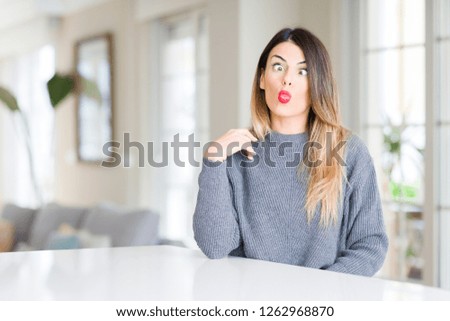 Young beautiful woman wearing winter sweater at home making fish face with lips, crazy and comical gesture. Funny expression.