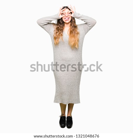 Young beautiful woman wearing winter dress doing ok gesture like binoculars sticking tongue out, eyes looking through fingers. Crazy expression.
