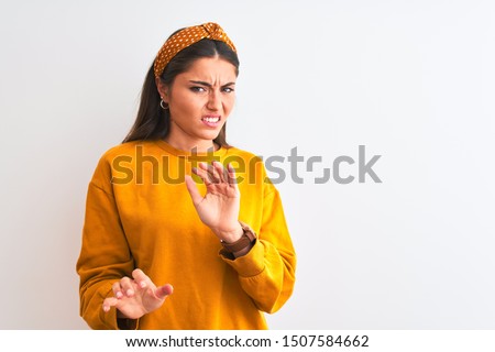 Young beautiful woman wearing yellow sweater and diadem over isolated white background disgusted expression, displeased and fearful doing disgust face because aversion reaction. With hands raised. 