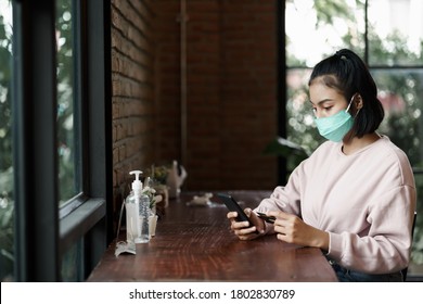 Young Beautiful Woman Wears Face Mask To Prevent COVID-19 While Chill Out And Make Payment Through Credit Card And Smart Phone In Cafe. Stock Photo