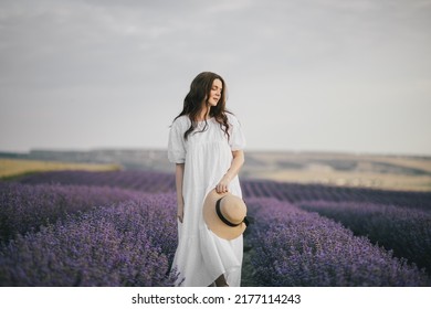 Young beautiful woman in white dress enjoying flower fragrance on lavender field.