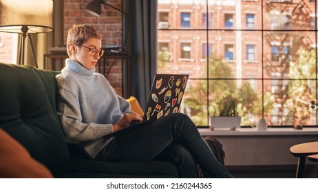 Young Beautiful Woman Working from Home on Laptop Computer with Stickers in Sunny Stylish Loft Apartment. Creative Female Checking Social Media, Browsing Internet. Urban City View from Big Window.