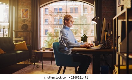 Young Beautiful Woman Working from Home on Desktop Computer in Sunny Stylish Loft Apartment. Creative Female Checking Social Media, Browsing Internet. Urban City View from Big Window.