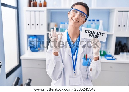 Young beautiful woman working on cruelty free laboratory doing ok sign with fingers, smiling friendly gesturing excellent symbol 