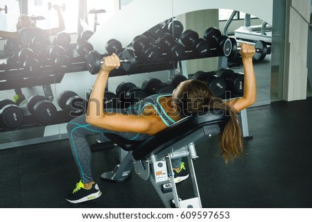 Young and beautiful woman working out with dumbbells in gym
