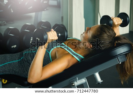 Young and beautiful woman working out with dumbbells in gym