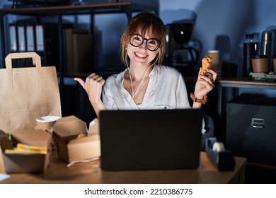 Young Beautiful Woman Working Using Computer Laptop And Eating Delivery Food Pointing To The Back Behind With Hand And Thumbs Up, Smiling Confident 