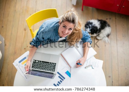 Young beautiful woman works on computer from a home with a laptop on a white desk as a freelancer.
Self-employment concept. Top view
