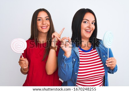 Young beautiful women holding sweet lollipop standing over isolated white background very happy pointing with hand and finger to the side
