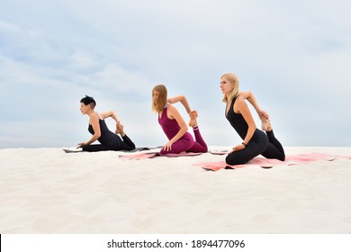Young beautiful women perform yoga exercises on the beach