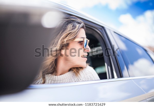 Young and beautiful women singing and dancing to\
the rhythm of music in their car, one woman looking back through\
the window