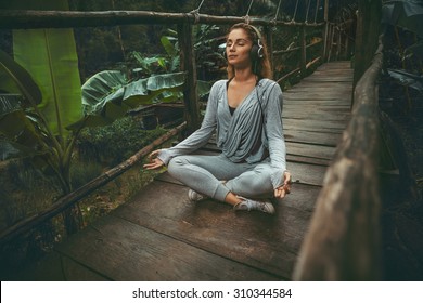 Young beautiful yoga woman listen to the music on suspension bridge in the tropic forest - Powered by Shutterstock