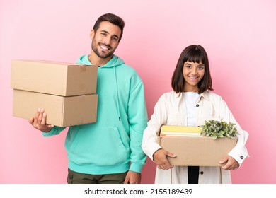 Young Beauty Couple Moving In New Home Among Boxes Isolated On Pink Background Posing With Arms At Hip And Smiling