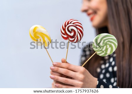 Young beauty in dotted shirt with three lollipops in hands. Cheerful lady with candies over white background.