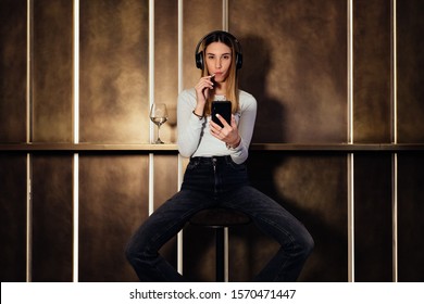 young beauty girl listening music on gold background. Sexy woman listening to music on headphones and licking lollipop. girl listening music on smartphone in a hotel.