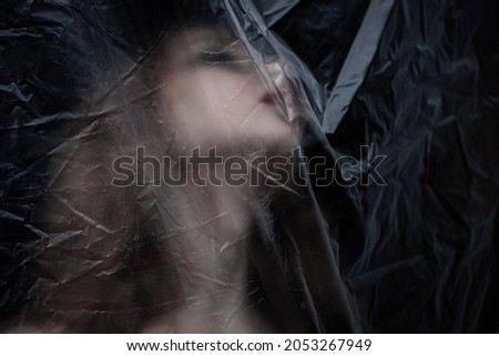 Young beauty sad woman trapped behind a plastic sheet as protection against COVID-19. Nicely fits for book cover 