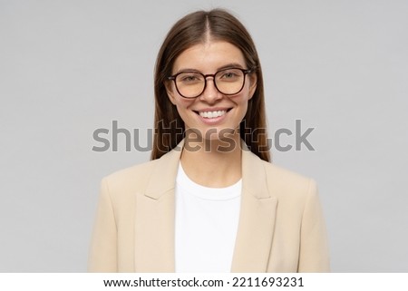 Young best brilliant student girl in stylish jacket and glasses looking at camera with candid smile on gray background. Youth, education and studying