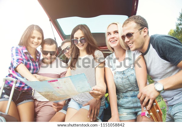 The young best friends with suitcases on a trip
by car. They sit in the back of the car, they look at the map,
resting after a long drive and having fun. Hitchhiking and car
trips with friends